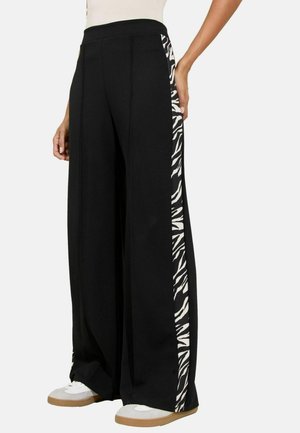 Pantaloni neri a gamba larga con un pannello laterale a strisce di zebra, realizzati in un tessuto morbido, con vita regolabile tramite cordoncino e dettagli bianchi a contrasto.