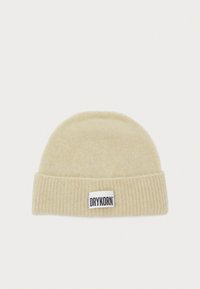 Chapeau en tricot de couleur beige clair avec une texture côtelée. Il présente une étiquette blanche avec "DRYKORN" en lettres noires sur le devant.