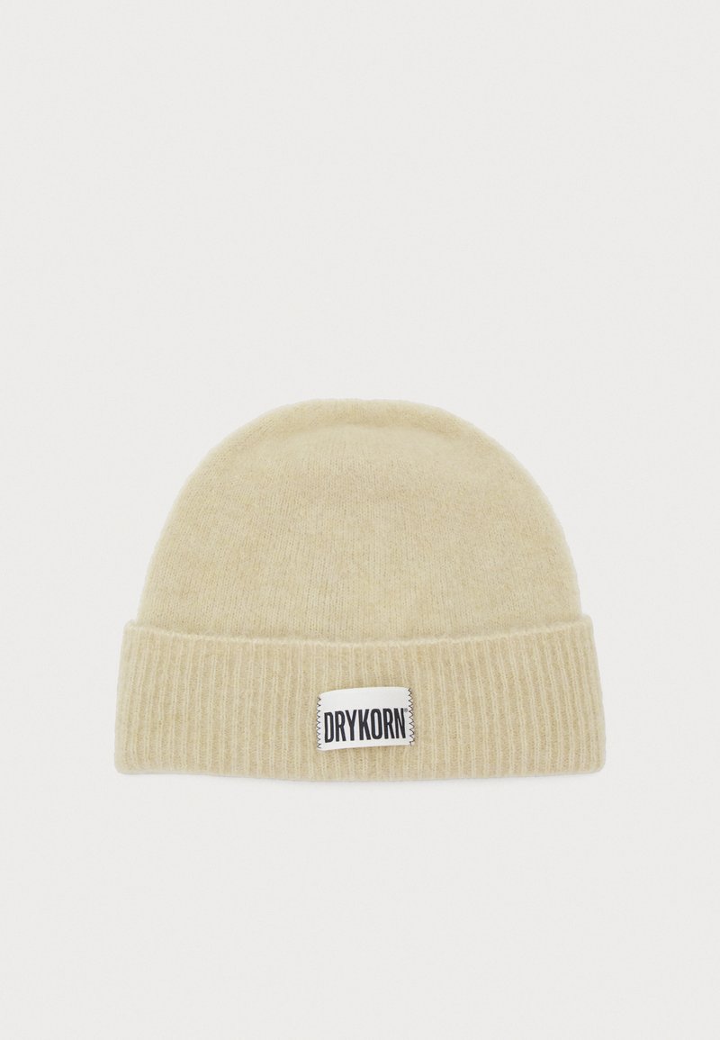 Chapeau en tricot de couleur beige clair avec une texture côtelée. Il présente une étiquette blanche avec "DRYKORN" en lettres noires sur le devant.
