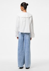 Weiße Baumwollbluse mit rüschenbesetztem Kragen und taillierten Manschetten, kombiniert mit weit geschnittenen blauen Jeans. Das Outfit hat eine lockere Passform.