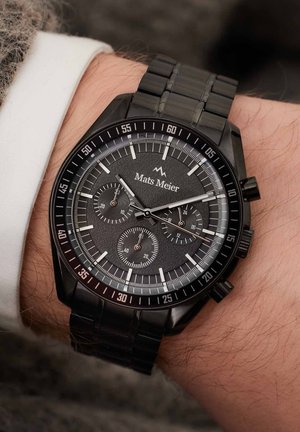 Montre chronographe noire avec un cadran texturé sombre, des accents argentés et un bracelet en métal. Elle comporte trois sous-cadrans et une échelle tachymétrique.