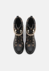 Bottes montantes noires à motif avec des accents de chaînes dorées, des clous décoratifs et une finition texturée. Bout en caoutchouc pour la durabilité.