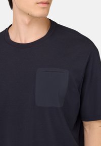 Námořnicky modré bavlněné tričko s kulatým výstřihem a texturovanou náprsní kapsou na levé straně hrudi. Krátké rukávy a hladký povrch.