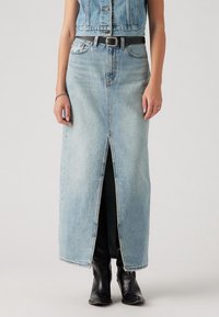 Denim-Maxi-Rock, hellblaue Waschung, hoher Schlitz vorne, abgeschlossener Saum, kombiniert mit einem schwarzen Gürtel und schwarzen kniehohen Stiefeln.