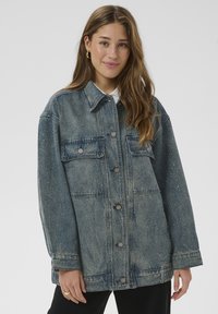 Jeansjacke in ausgeblichenem Blau mit übergroßem Schnitt, silbernen Punktakzenten, zwei Brusttaschen und vorderer Knopfleiste. Lange Ärmel und stabiler Kragen.