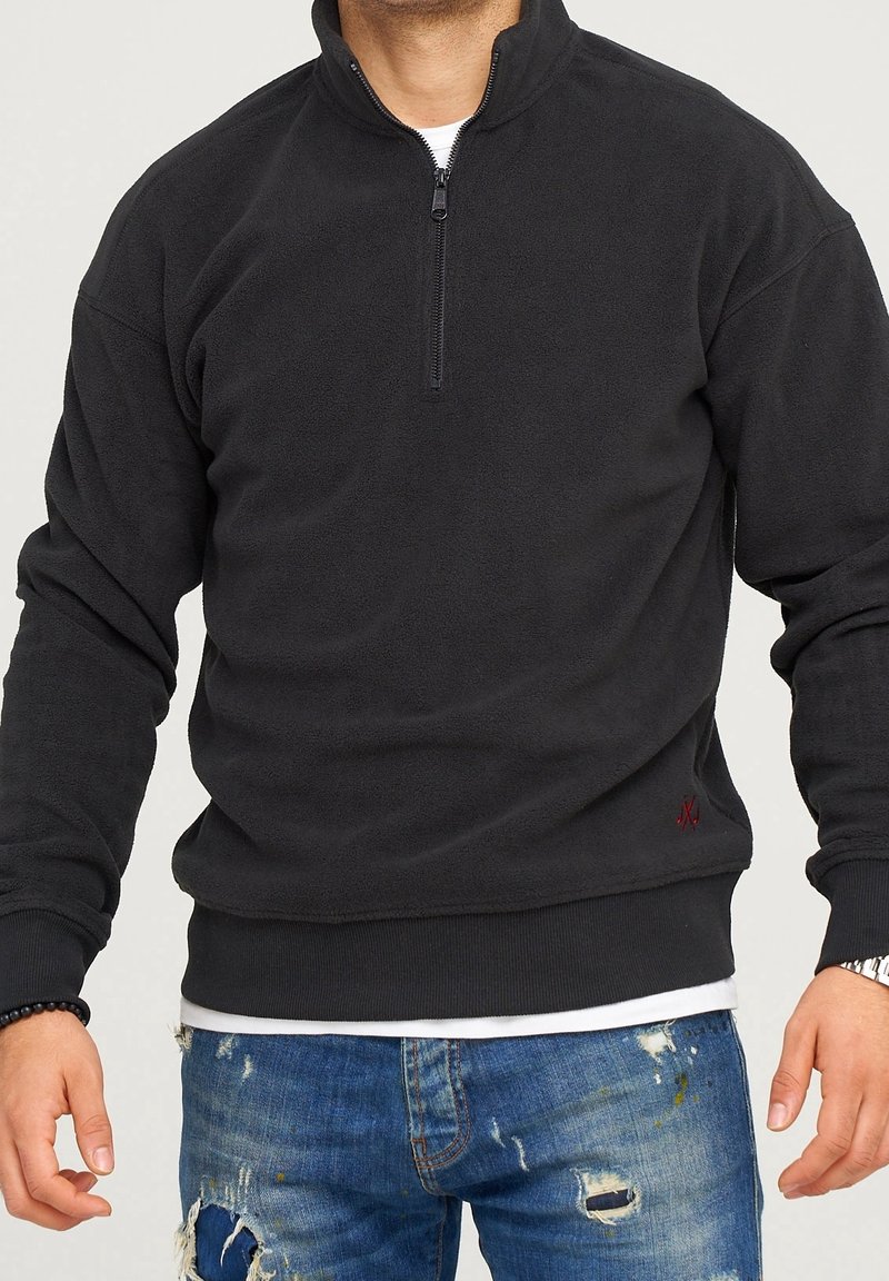 Pullover in pile nero con colletto a mezza zip, dotato di polsini e orlo a coste. Dettaglio logo rosso discreto in basso a sinistra. Vestibilità casual.