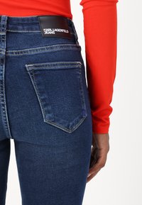 Mörkblå denimjeans med hög midja, med bakfickor och en svart läderetikett med "KARL LAGERFELD JEANS" prägling.