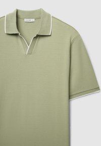 Polo vert clair en tissu texturé, comportant un col en V, des manches courtes et une bordure blanche le long du col et des manches. Étiquette de la marque visible.