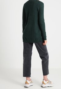 Dark green long-sleeve sweater with a relaxed fit, paired with dark gray tapered pants and multicolored sneakers; smooth texture.