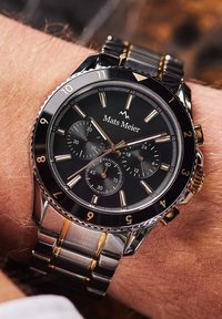 Montre bracelet bicolore argent et or avec un cadran noir, des sous-cadrans chronographe, de grands index horaires et un bracelet en acier inoxydable.