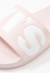 Rózsaszín csúszós papucs, texturált felsőrésszel, nagy fehér betűkkel. Puha anyag, lapos talp és minimális varrási részletek.