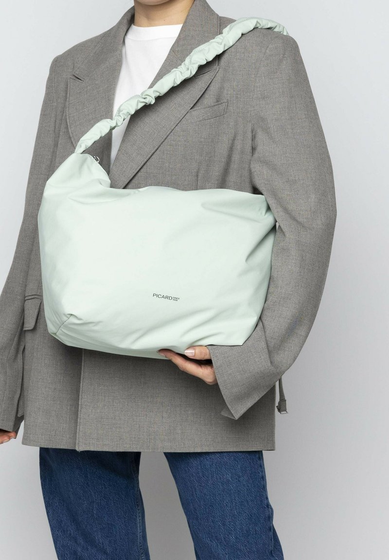 Helles grünes Schultertasche aus glattem Material, mit einem gerafften Tragegurt und subtiler Markenkennzeichnung. Getragen mit einem grauen Oversized-Blazer.
