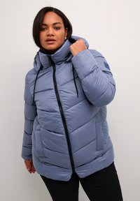 Giacca a vento azzurro chiaro con cappuccio, caratterizzata da cuciture verticali, zipper frontale e coulisse regolabili. Tasche laterali incluse.