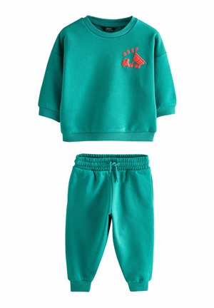 Komplet v modrozeleni barvi, sestavljen iz športne majice in usklajenih hlač. Športna majica ima na prsih rdeč risani motiv vozila. Narejeno iz mehkih, raztegljivih materialov.