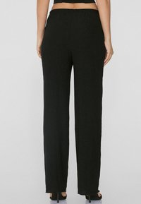 Pantalon large noir en tissu texturé, avec une taille élastique et des détails à ourlet brut, montré de dos.