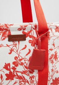 Sac fourre-tout blanc avec imprimé floral rouge, poignées rouges et étiquette en cuir rouge embossée avec le logo "Marc O’Polo".
