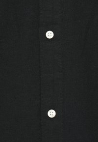 Μαύρο πουκάμισο με κουμπιά, με απλή ύφανση και λευκή λεπτομέρεια κουμπιού στο λάστιχο, με ευθείες ραφές κατά μήκος των άκρων.