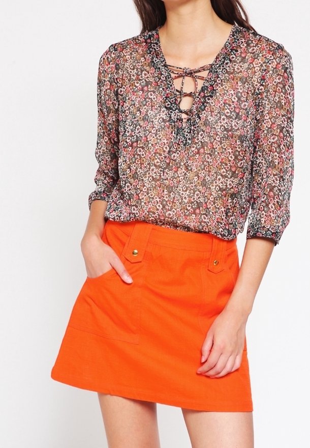 Blouse transparente à motif floral avec encolure à lacets ; associée à une jupe trapèze orange unie avec poches avant et détails en métal doré.
