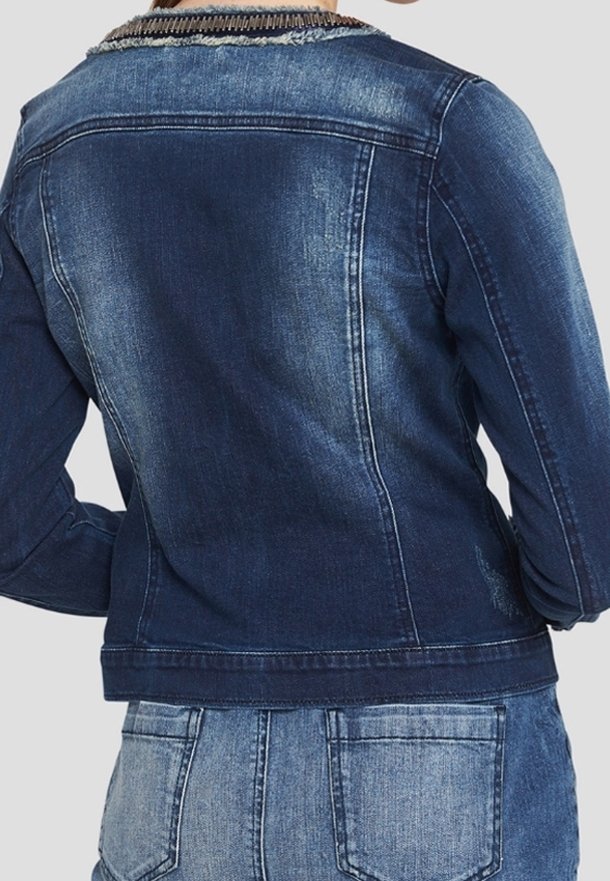 Vista posteriore di una persona che indossa una giacca di jeans blu scuro sbiadita su jeans di denim azzurro contro uno sfondo semplice.