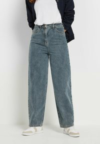 Hoge taille wijde spijkerbroek in vervaagd blauw, met een knoopsluiting, vijf zakken en een onafgewerkte zoom, gecombineerd met witte sneakers.