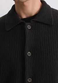 Black knitted cardigan with a ribbed texture, featuring a collar and five dark buttons along the front.