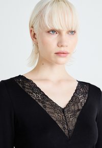 Top negru cu decolteu în V, având margini din dantelă florală. Țesătură netedă cu un design ajustat. Cercei simpli cu cercuri din argint.