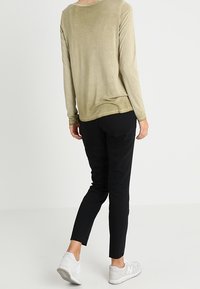 Top a maniche lunghe verde oliva con una vestibilità ampia, abbinato a pantaloni neri slim-fit e scarpe da ginnastica bianche, che mostra un look informale.