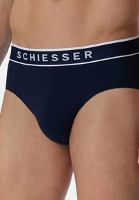 Slip in cotone blu navy con una vita bianca che presenta il nome del marchio "SCHIESSER" in lettere in grassetto. Texture liscia, vestibilità classica.