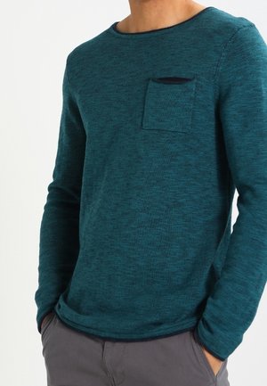 Türkisfarbenes Langarmshirt mit rundem Halsausschnitt, strukturierter Stoff und kleiner Brusttasche. Hat eng anliegende Ärmel und einen geraden Saum.