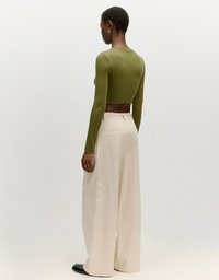 Olivgrünes, langärmeliges, cropped Oberteil kombiniert mit cremefarbenden, weit geschnittenen Hosen; beide besitzen glatte Texturen und ein minimalistisches Design.