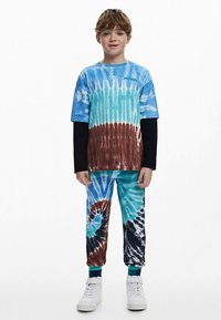 Blue and brown tie-dye t-shirt, black long-sleeve underneath, matching pants, and white sneakers. Textured fabric with swirl patterns.