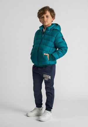 Teal puffer jacket with horizontal quilted design, zip closure, and hood; paired with navy sweatpants featuring "OREGON 1997" text, white sneakers.