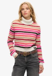 Pull en rayures de teintes rose, beige et marron ; doté d'un col montant côtelé et de poignets côtelés ; porté sur un jean taille haute avec une ceinture.