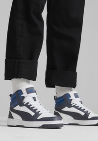 Zapatillas altas con una combinación de colores blanca, navy y azul. Materiales de cuero y sintético, puntera perforada, collar acolchado y suela de goma.