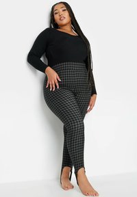 Top negro de mangas largas combinado con leggins de cintura alta con un patrón de hilo de pajarito en negro y gris. Detalle en forma de corte en los tobillos.