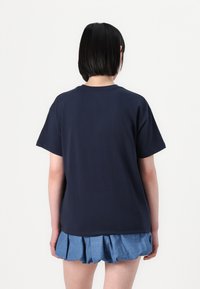 Navy blue cotton t-shirt with short sleeves, rounded neckline, and loose fit, paired with a layered blue skirt with ruffles.