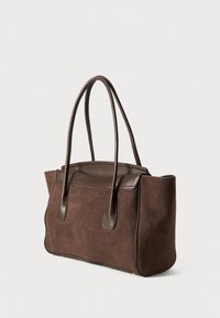Sac fourre-tout en daim marron avec des accents en cuir foncé, doté de deux poignées allongées, d'une forme structurée et d'une finition lisse et élégante.