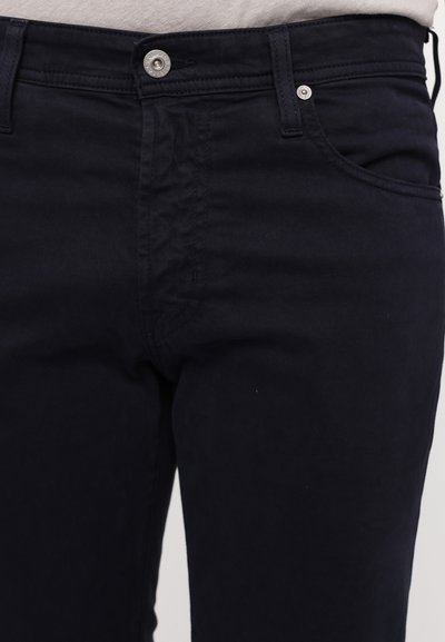 Σκούρο μπλε τζιν από βαμβάκι με παραδοσιακό σχέδιο πέντε τσεπών, μεταλλικό κλείσιμο με κουμπί και αντίθετη ραφή κατά μήκος των ραφών.