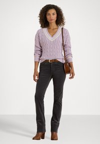 Lilac cable-knit sweater with a V-neck and cream trim, paired with dark gray corduroy pants and brown heeled ankle boots, accessorized with a brown bag.