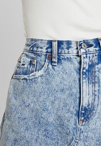 Jeans in denim blu a vita alta con motivo scolorito, cuciture a contrasto, chiusura con bottone e dettagli usurati sulla tasca.