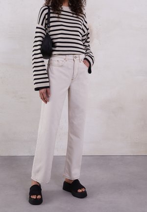 Suéter de punto a rayas en negro y crema, jeans crema de cintura alta y sandalias de plataforma negras. Presenta mangas anchas y dobladillo deshilachado en los jeans.