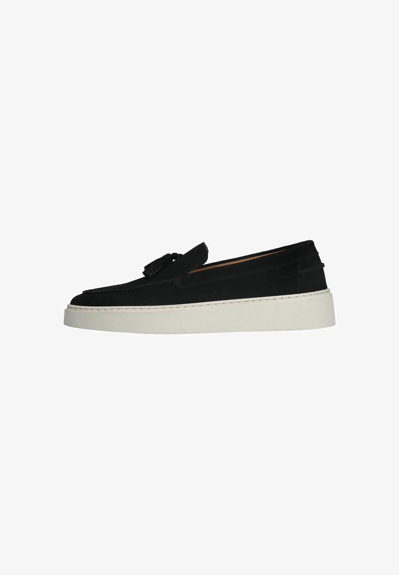 Black suede slip-on shoes with a rounded toe, tassel detail, and a white thick sole. Features stitching along the sole.
