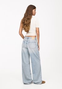 Světle modré džíny s širokými nohavicemi s vybledlým efektem, pěti kapsami a hnědou nášivkou na pasu. Kombinované s přiléhavým krémovým topem.