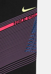 Ropa deportiva negra con un diseño estampado que incluye líneas en rosa, morado y azul. Incluye el logotipo de Nike Pro en rojo y una marca de verificación amarilla.