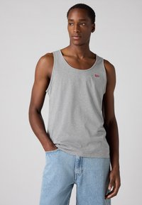 Débardeur en coton gris avec un col rond, arborant un petit logo rouge. Associé à un short en denim bleu clair. Texture lisse.