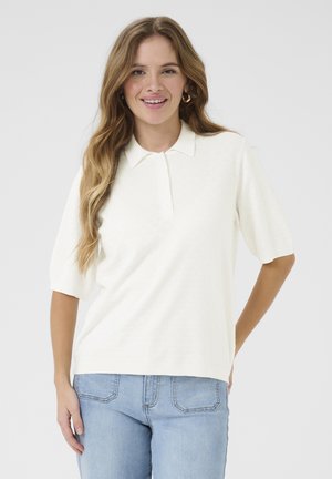 Cremefarbiges Poloshirt mit kurzen Ärmeln aus weichem Stoff, Knopfleiste und geripptem Kragen, kombiniert mit hellblauen high-waisted Jeans.