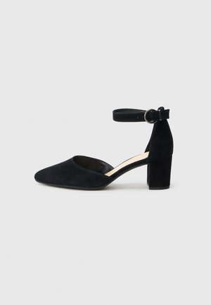 Black suede high-heeled shoe with a pointed toe, ankle strap featuring a buckle, and a block heel. Smooth texture, minimalistic design.