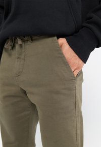 Pantalons vert olive en coton, à coupe classique, avec poches latérales et une taille à cordon de serrage, d'une texture lisse.