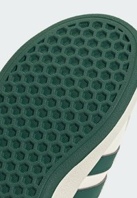 Green rubber sole with a hexagonal pattern and textured surface. Accented by a cream edge and contrasting green stripes.