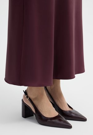 Piedi che indossano décolleté slingback a punta viola scuro sotto una gonna lunga coordinata.